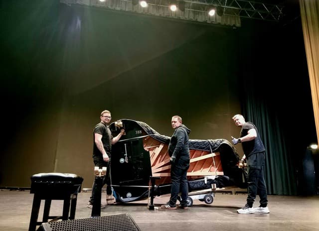 JJS Pianos crew preparing a grand piano on a theatre stage